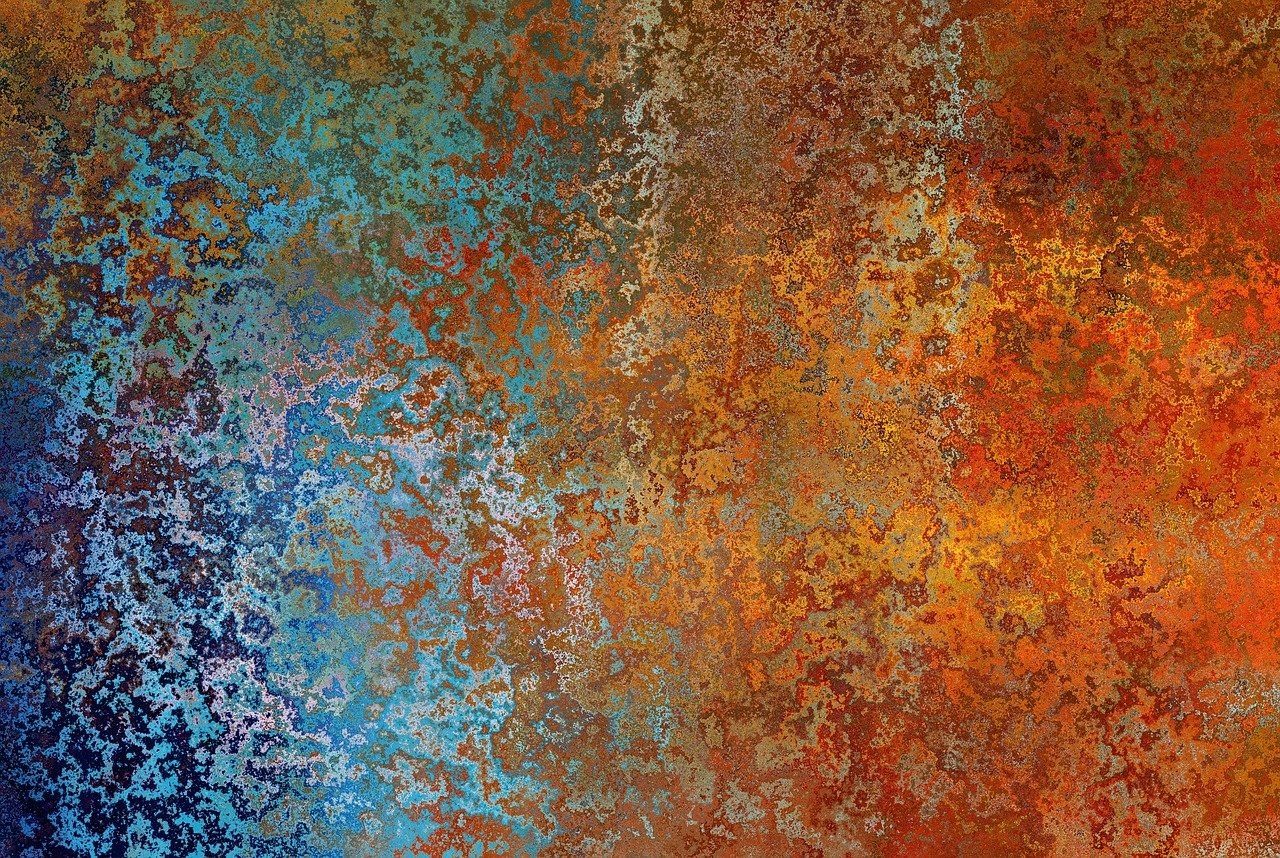 A mottled surface of corroded metal, deep blue and turquoise at the left turning to orange and red rust at the right.
