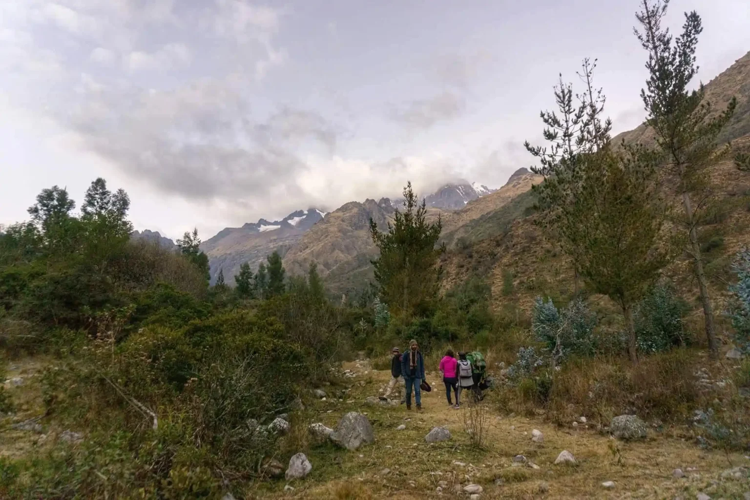 Four people standing together in a clearing below cloud covered peaks, small against the scale of the valley.