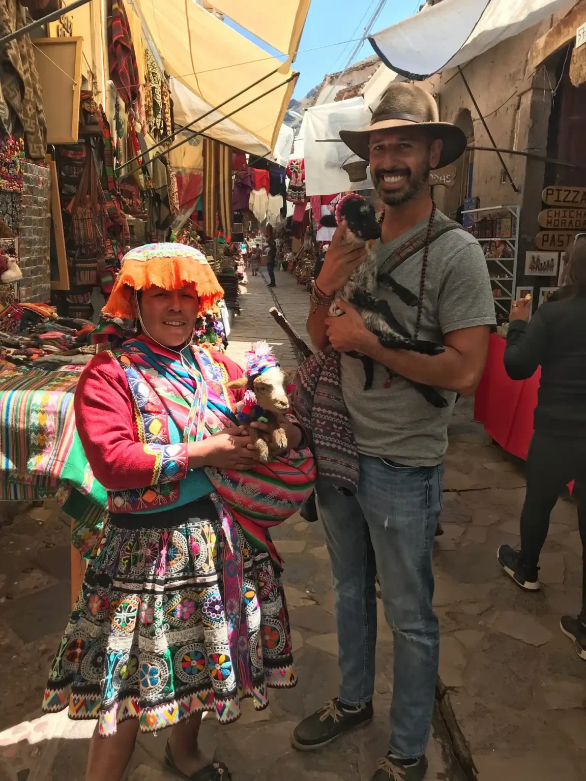 A Quechua woman in traditional dress and Hamid Jabbar standing in the Pisac market, each holding a young animal.
