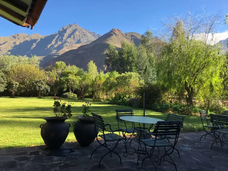 A stone terrace set with garden chairs and planted urns, looking across the lawn to the mountains.