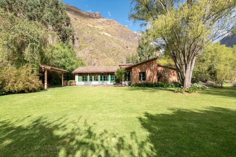 The villa's garden front, with green framed windows, a covered terrace and a wide lawn under the mountain.